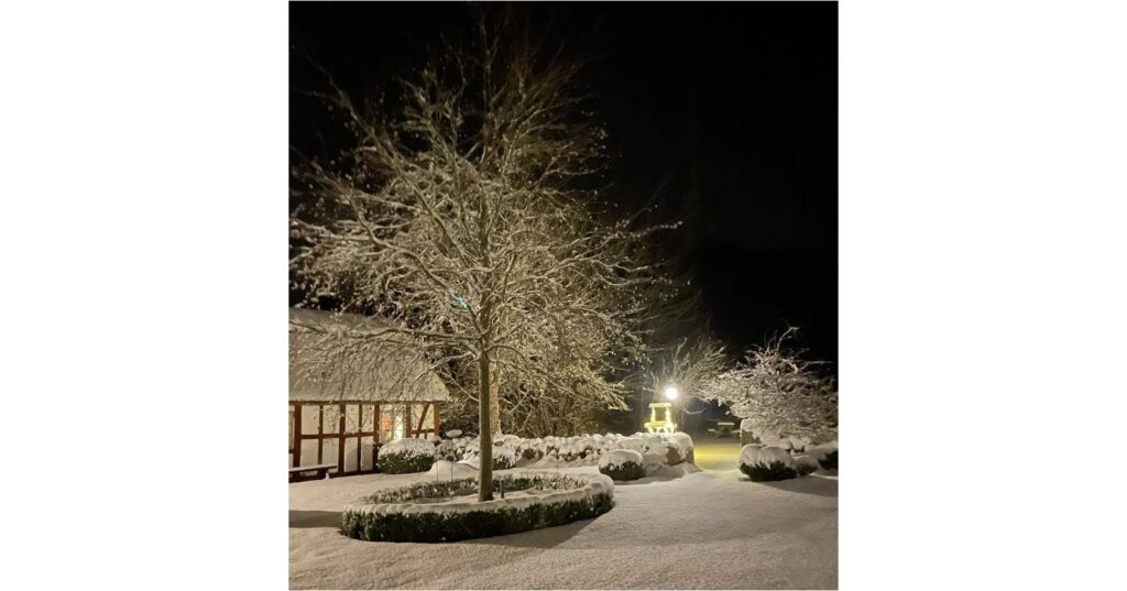 Bild på Drakamöllan Gårdshotell. Snön föll och ligger orörd på gården. Man ser gårdshuset, ett glittrande träd och en ljuskälla en bit bort.